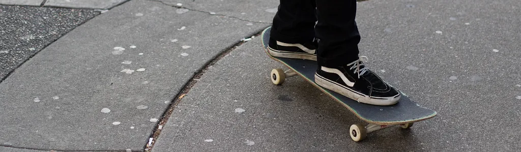 Young man riding his skateboard on gum stained concrete roadway
